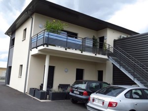Construction de bureaux avec garde corps et terrasse surélevé, voitures garées devant, par BELCASTRO.