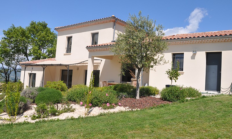 Maison à étage construite par Belcastro avec massif effet jardin japonais petits arbustes et galets blancs.