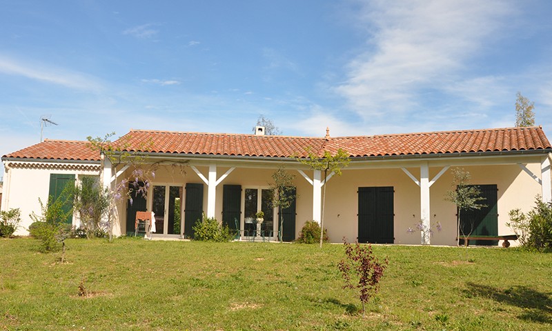 Vue de face d'une maison de plain pied avec volets noirs et grand jardin, une construction BELCASTRO.
