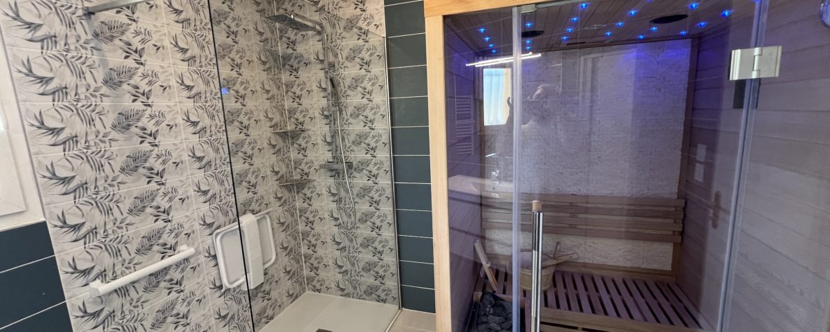 Une rénovation de salle de bains BELCASTRO avec une faience turquoise et grise et l'installatino d'un sauna aux portes vitrées.
