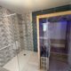 Une rénovation de salle de bains BELCASTRO avec une faience turquoise et grise et l'installatino d'un sauna aux portes vitrées.