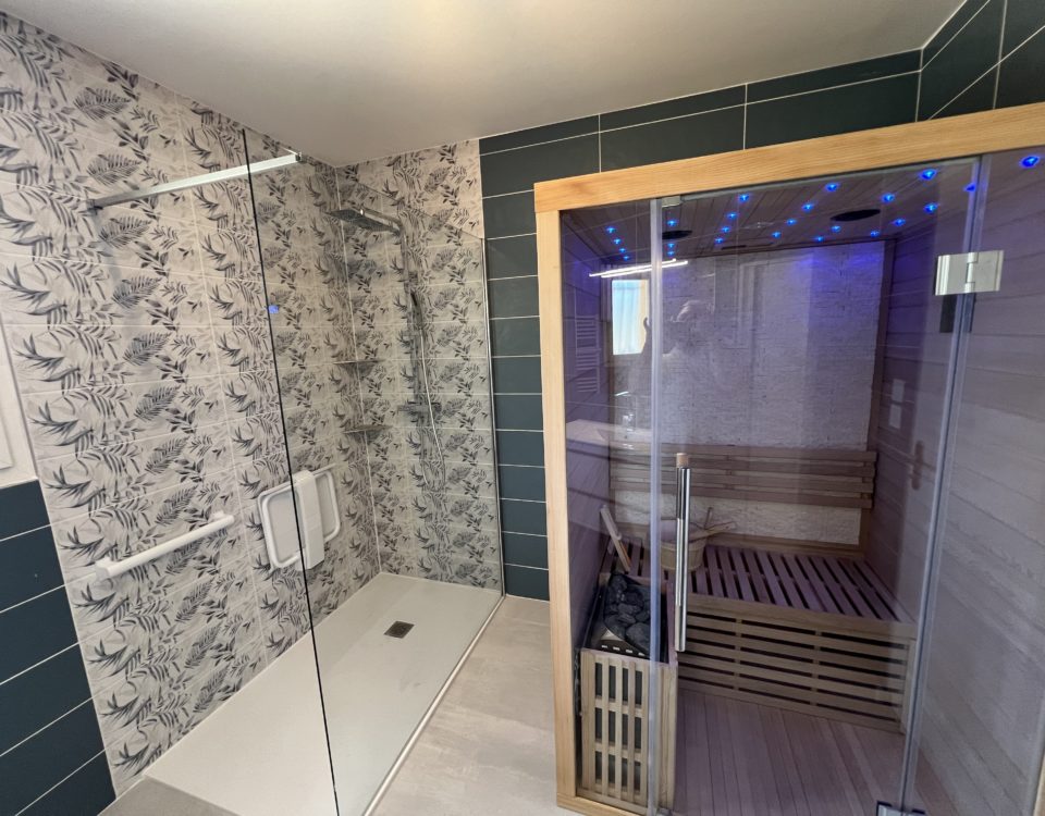 Une rénovation de salle de bains BELCASTRO avec une faience turquoise et grise et l'installatino d'un sauna aux portes vitrées.