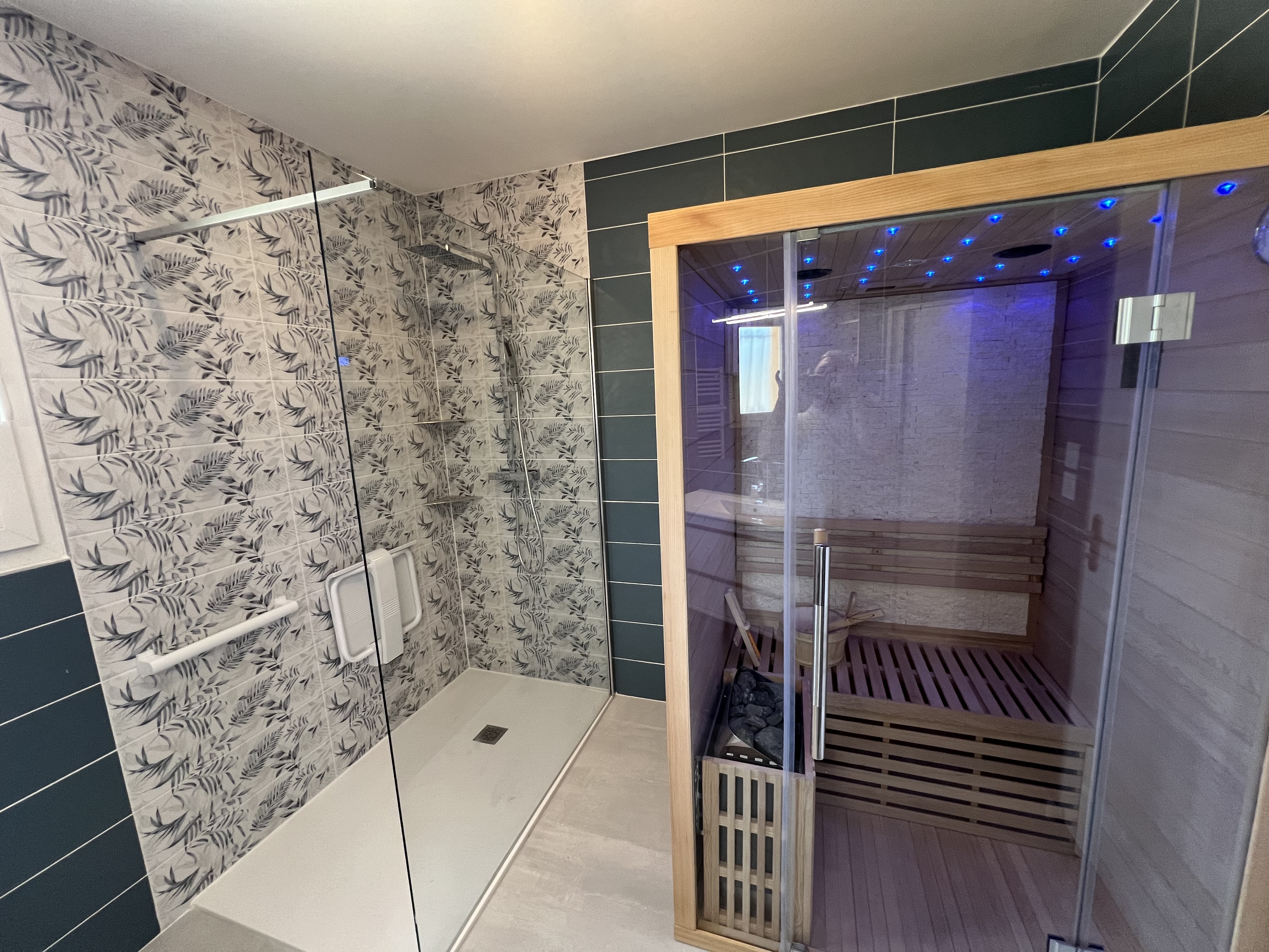 Une rénovation de salle de bains BELCASTRO avec une faience turquoise et grise et l'installatino d'un sauna aux portes vitrées.