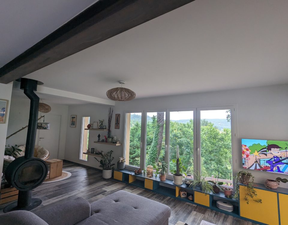 Une réalisation d'agrandissement salon avec grand espace lumineux et fenêtre, poêle, canapé gris par BELCASTRO.
