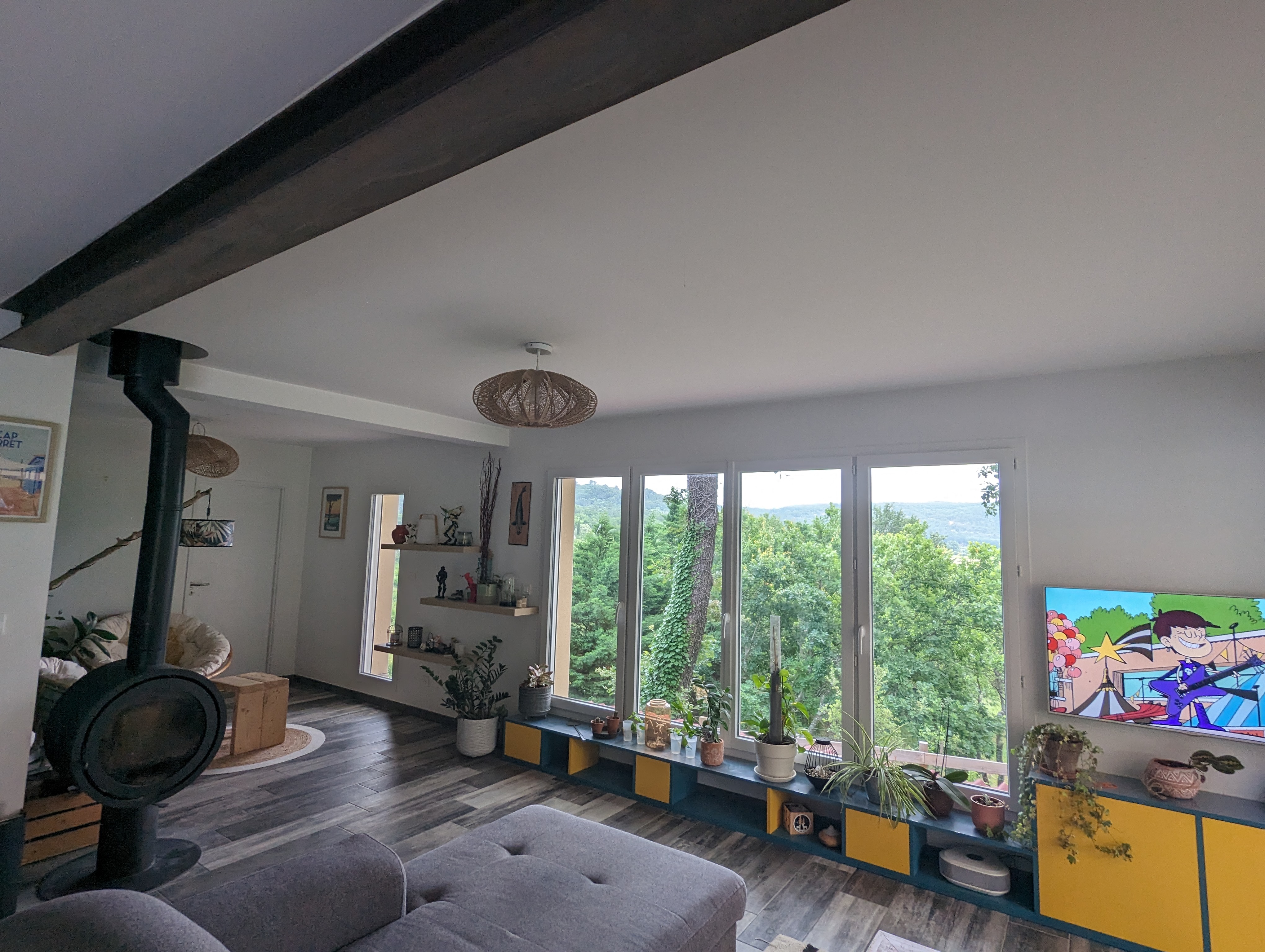 Une réalisation d'agrandissement salon avec grand espace lumineux et fenêtre, poêle, canapé gris par BELCASTRO.